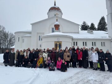 Ryhmä ihmisiä seisoo lumisessa maisemassa kirkon edustalla.