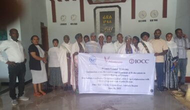 Ryhmä ihmisiä seisoo hotellin aulassa ja pitää banderollia. Seinällä on kelloja eri aikavyöhykkeille.