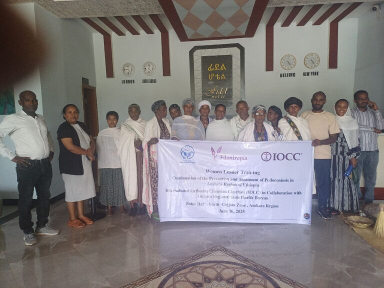 Ryhmä ihmisiä seisoo hotellin aulassa ja pitää banderollia. Seinällä on kelloja eri aikavyöhykkeille.