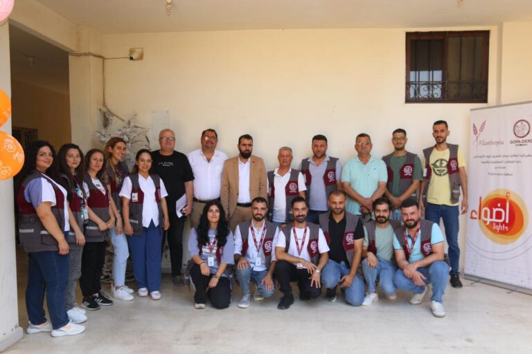 Ryhmä ihmisiä seisoo ja istuu sisätiloissa mainoskylttien edessä, useilla on yllään virkapuvut.