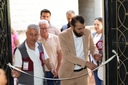 Mies leikkaa valkoista nauhaa juhlallisessa tilaisuudessa, ympärillä seisoo ihmisiä virallisissa asuissa.