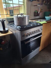 Kattila kiehuu kaasuliedellä, vieressä vedenkeitin ja tiskiallas. Ikkunasta näkyy piharakennus.