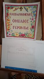 Kaksiosainen, käsinkirjoitettu juliste, jossa on kreikkalaista ja englantilaista tekstiä sekä kukkakuvioita.