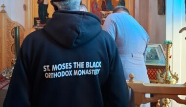 Mies ortodoksikirkossa, jossa on ikoneja ja koristeellisia puuleikkauksia. Hupparissa lukee St. Moses the Black.