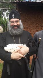 Mies ortodoksisessa asussa pitää sylissään pientä mustavalkoista karitsaa, taustalla savimaja.