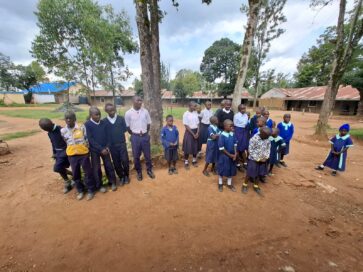 Ryhmällinen lapsia eri ikäryhmistä seisoo ulkona koulun pihalla.
