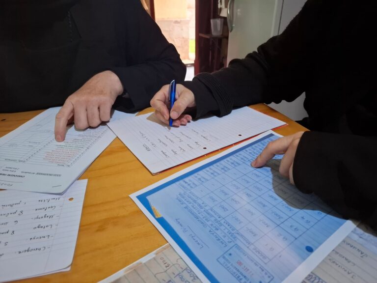 Kaksi henkilöä tarkistaa ja kirjoittaa muistiinpanoja kirjanpitoon pöydän ääressä.